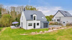 A modern two-story house with a sloped roof, a covered patio with outdoor furniture, and a well-maintained lawn. - Discovering the Breton Riviera- House for 8 (La Forêt-Fouesnant)