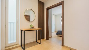 A hallway with a wooden table, a round mirror, and a sliding door leading to a bedroom.