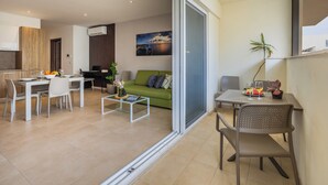 A modern living room with a green sofa, a dining area with a white table and chairs, and a kitchen with wooden cabinets.
