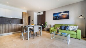 A modern living room with a green sofa, a dining table with chairs, a coffee table, and a painting on the wall.