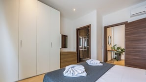 A hotel room with a bed, a wardrobe, a mirror, and a potted plant. - Family-friendly apartment near Ghadira, Paradise & Golden Bay Modern amenities & coin-operated A/C Perfect base for your Malta beach getaway. (Il-Mellieħa)