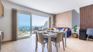 A modern living room with a dining area, large sliding glass doors, and a view of the city. - Family-friendly apartment near Ghadira, Paradise & Golden Bay Modern amenities & coin-operated A/C Perfect base for your Malta beach getaway. (Il-Mellieħa)