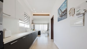 A modern kitchen with dark cabinets, a white countertop, and a dining area in the background.