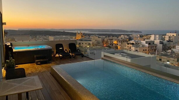 Piscina infinita en la azotea con vistas a un paisaje urbano al atardecer.