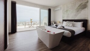 Habitación de hotel moderna con una bañera grande, una cama con ropa blanca y vistas a la ciudad a través de la puerta de cristal.