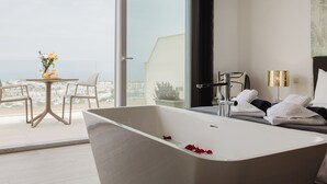 Un baño moderno con una bañera independiente, un balcón con cerramiento de vidrio con mesa y sillas, y vistas a la ciudad.