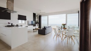 Una cocina moderna con una isla central, un comedor con mesa de vidrio y una sala de estar con sofá.