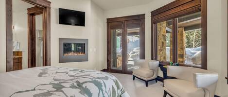Un dormitorio con una cama grande, una chimenea, un televisor y vistas al exterior.
