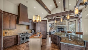 A spacious kitchen with dark wood cabinets, a large island, and a stone fireplace. - Snow Meadow at The Colony (Park City)