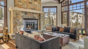 A spacious living room with a stone fireplace, large windows offering mountain views, and a cozy seating area. - Snow Meadow at The Colony (Park City)