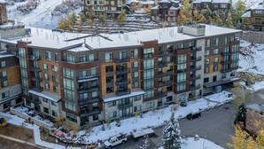A modern multi-story building with large windows and balconies, surrounded by snow-covered hills and a clear sky. - Lift Condo With Ski-in out w Village Access hot tub Fitness Center ski Rentals On-site (Park City)