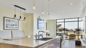 A modern kitchen with a central island, pendant lighting, and a view of neighboring houses through large windows. - Lift Condo With Ski-in out w Village Access hot tub Fitness Center ski Rentals On-site (Park City)
