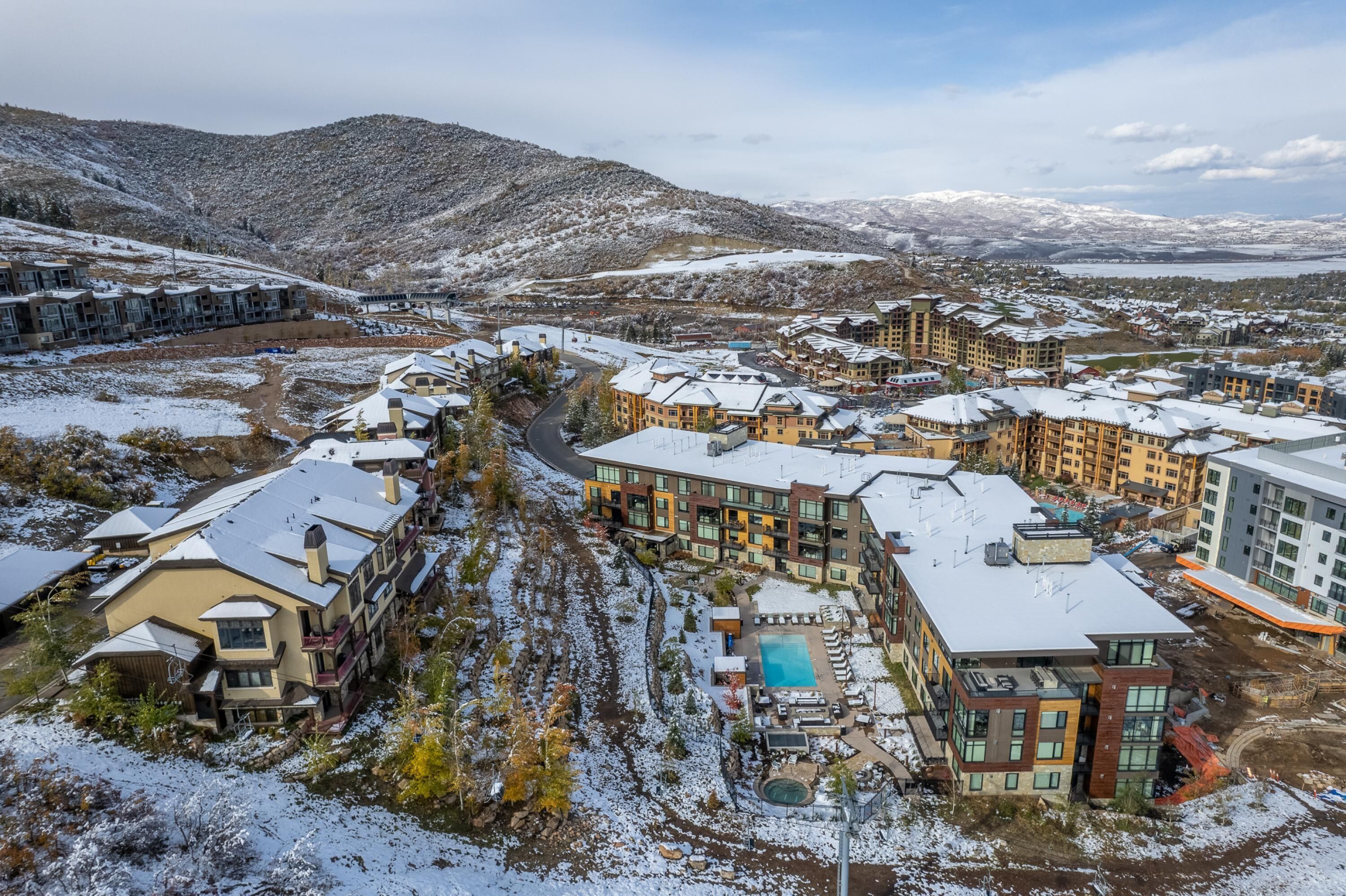Estância coberta de neve com vários edifícios, uma piscina e montanhas ao fundo.