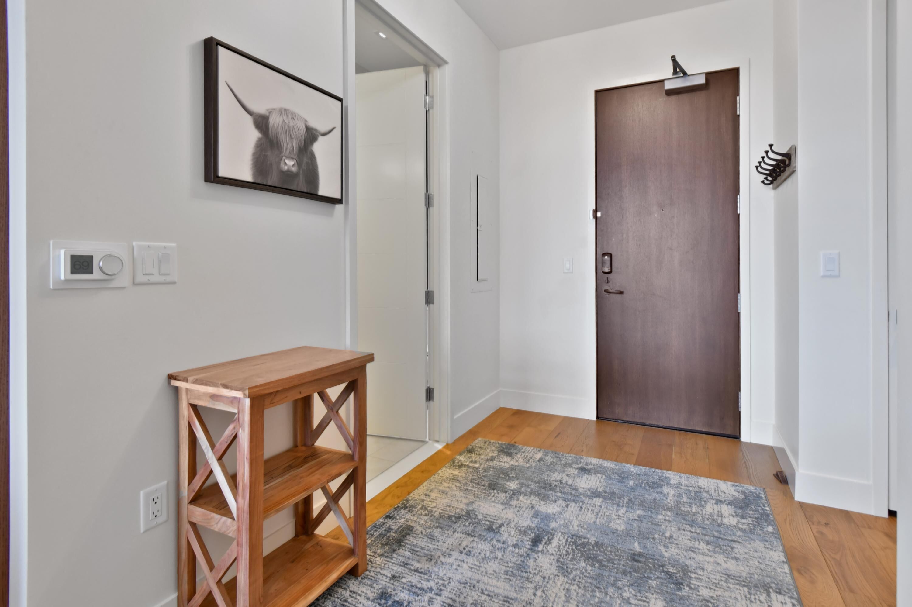 A hallway with a wooden console table, a framed picture of a yak, a door, and a wall-mounted light switch.