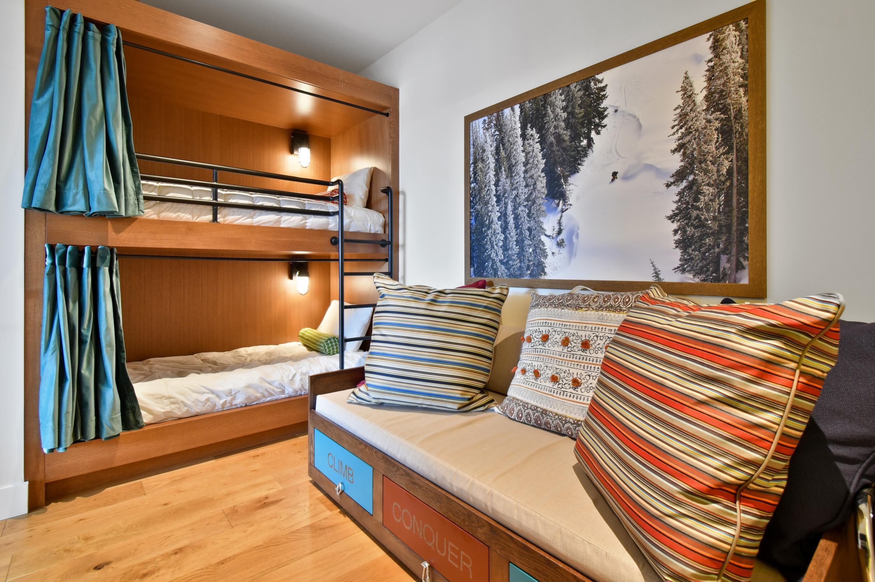 A room with a bunk bed, a sofa with patterned cushions, and a large framed picture of a snowy forest.