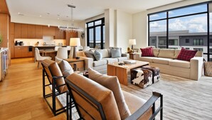 Un salon moderne avec un canapé, des fauteuils, une table basse et une vue sur la ville grâce à de grandes fenêtres.
