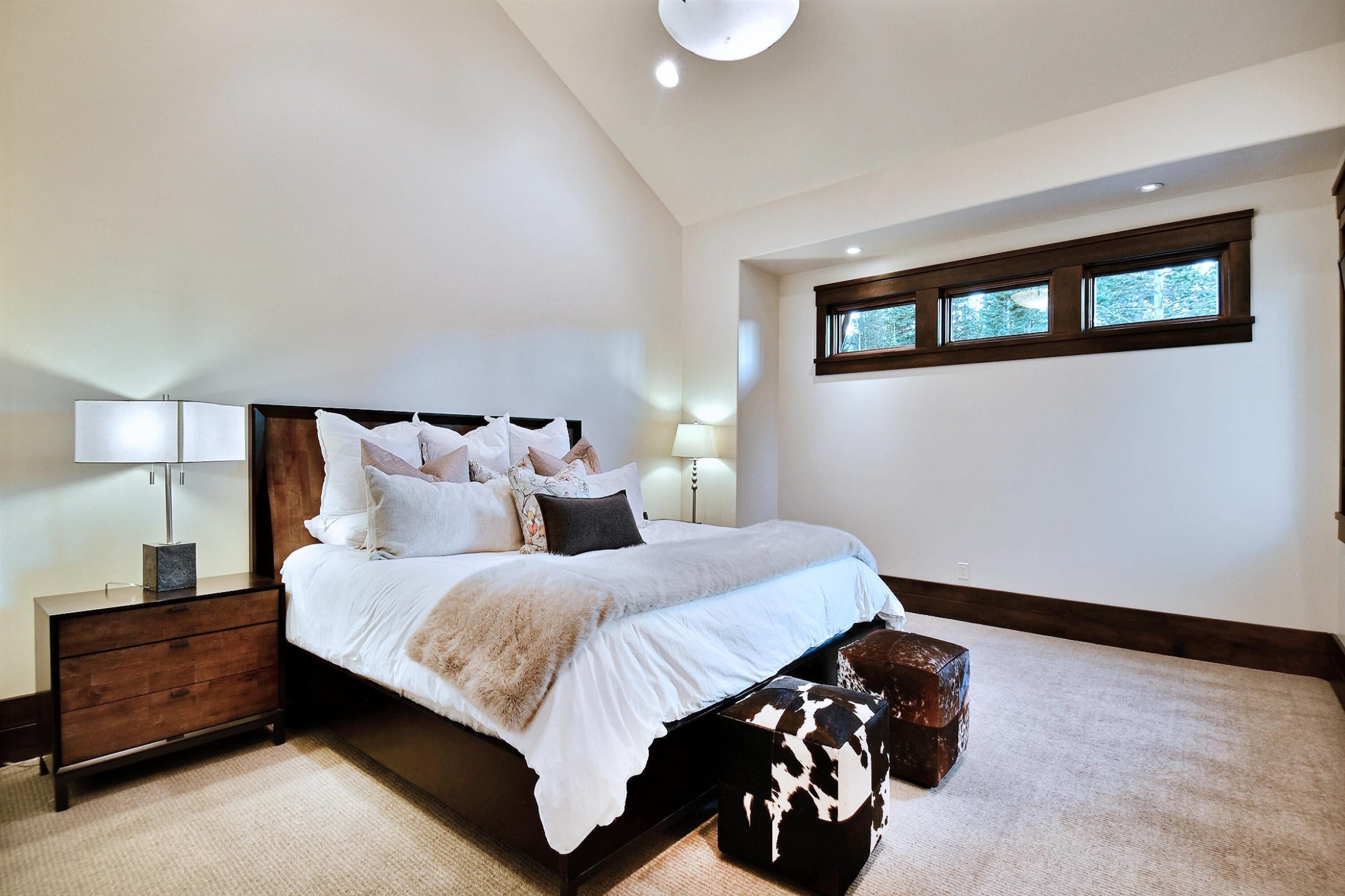 Une chambre à coucher avec un grand lit, une table de chevet, une lampe et une fenêtre.
