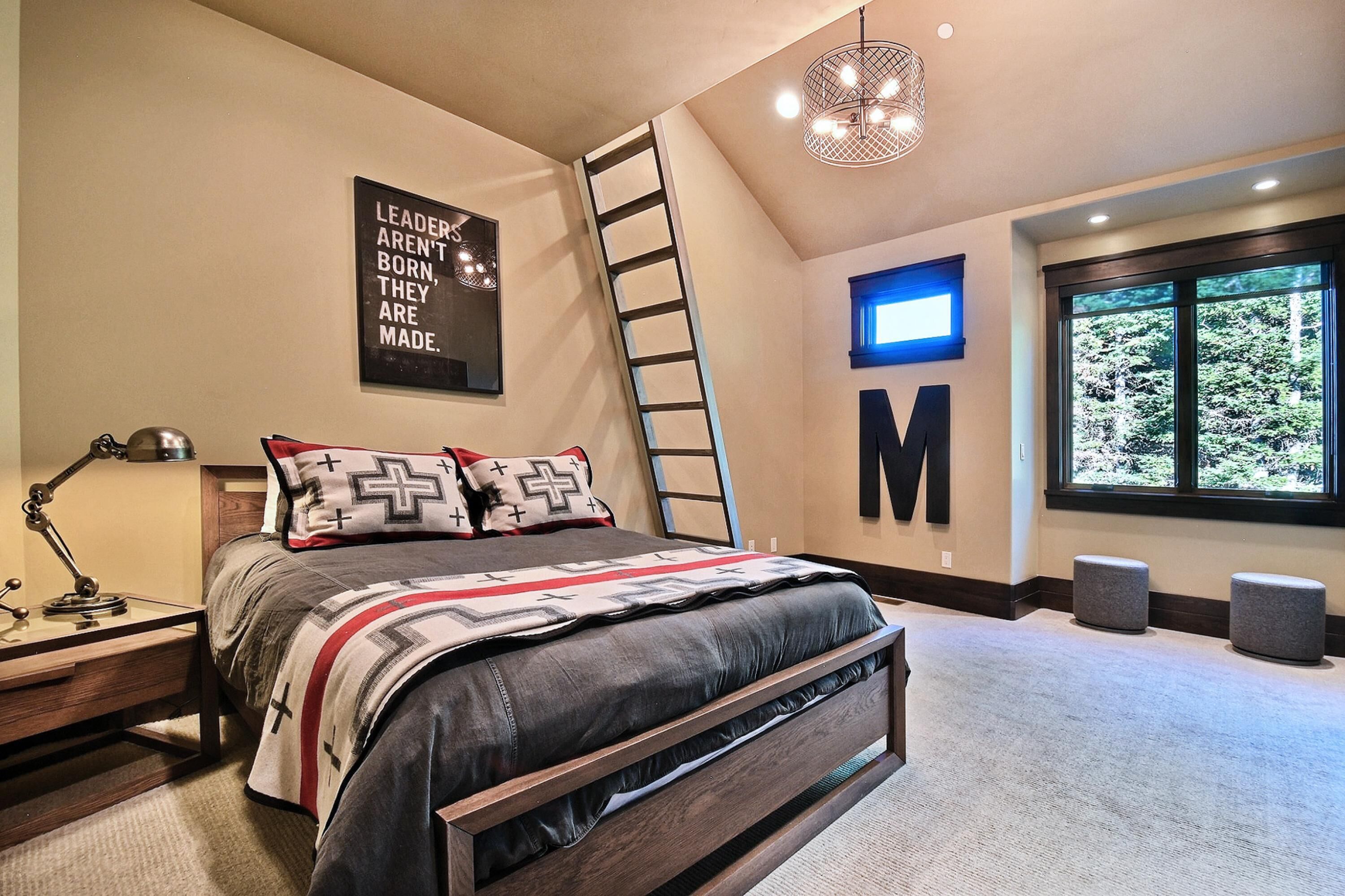 A bedroom with a bed, a ladder, a desk with a lamp, a large window with a view, and a motivational quote on the wall.