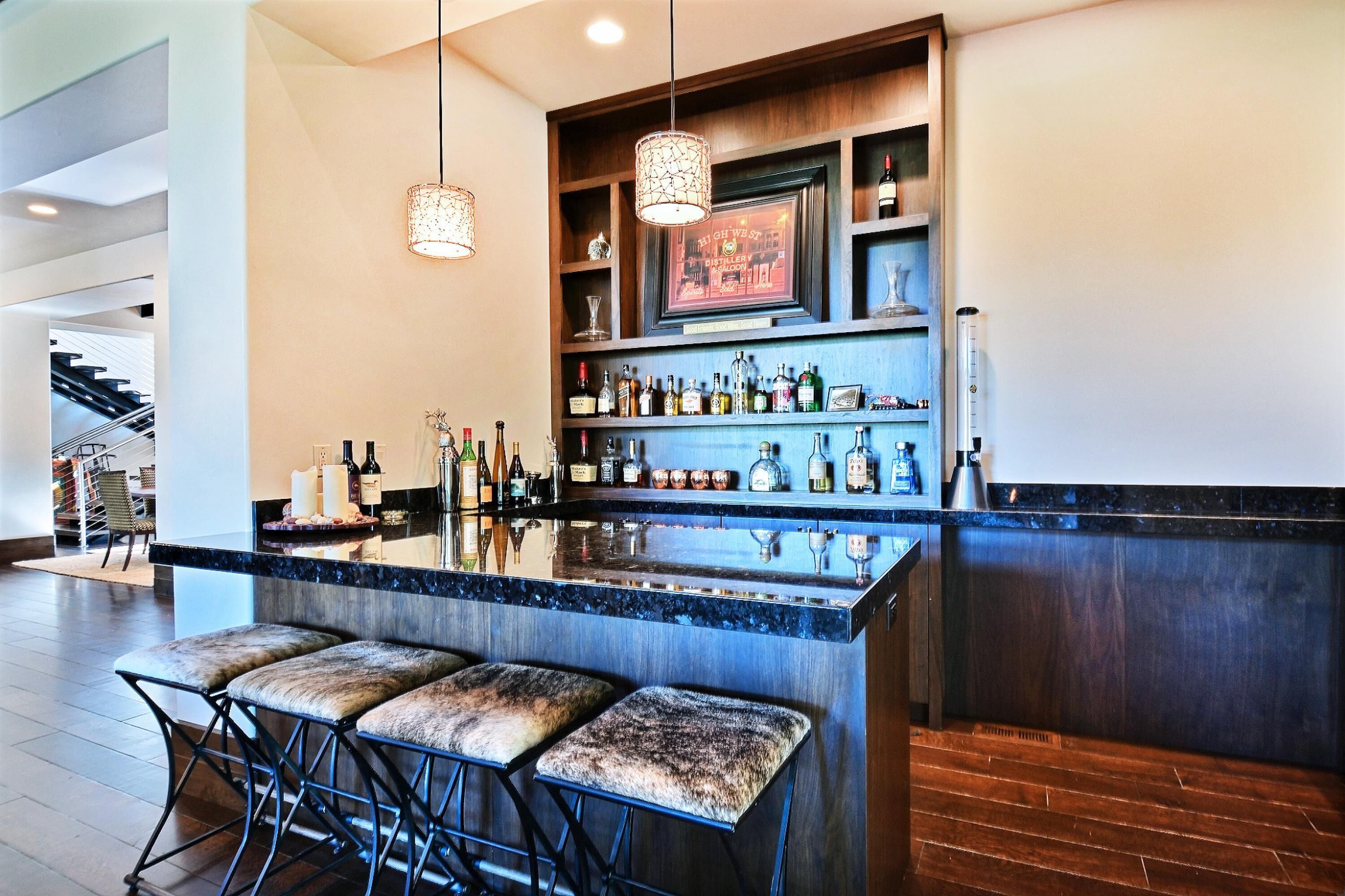 A modern bar area with a marble countertop, multiple liquor bottles, and bar stools.
