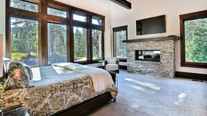 A spacious bedroom with a large bed, a stone fireplace, and large windows offering a forest view. - Chic Colony Ski-in Ski Out Villa Direct Access to Adventures at Park City Resort Hot Tub Gym (Park City)