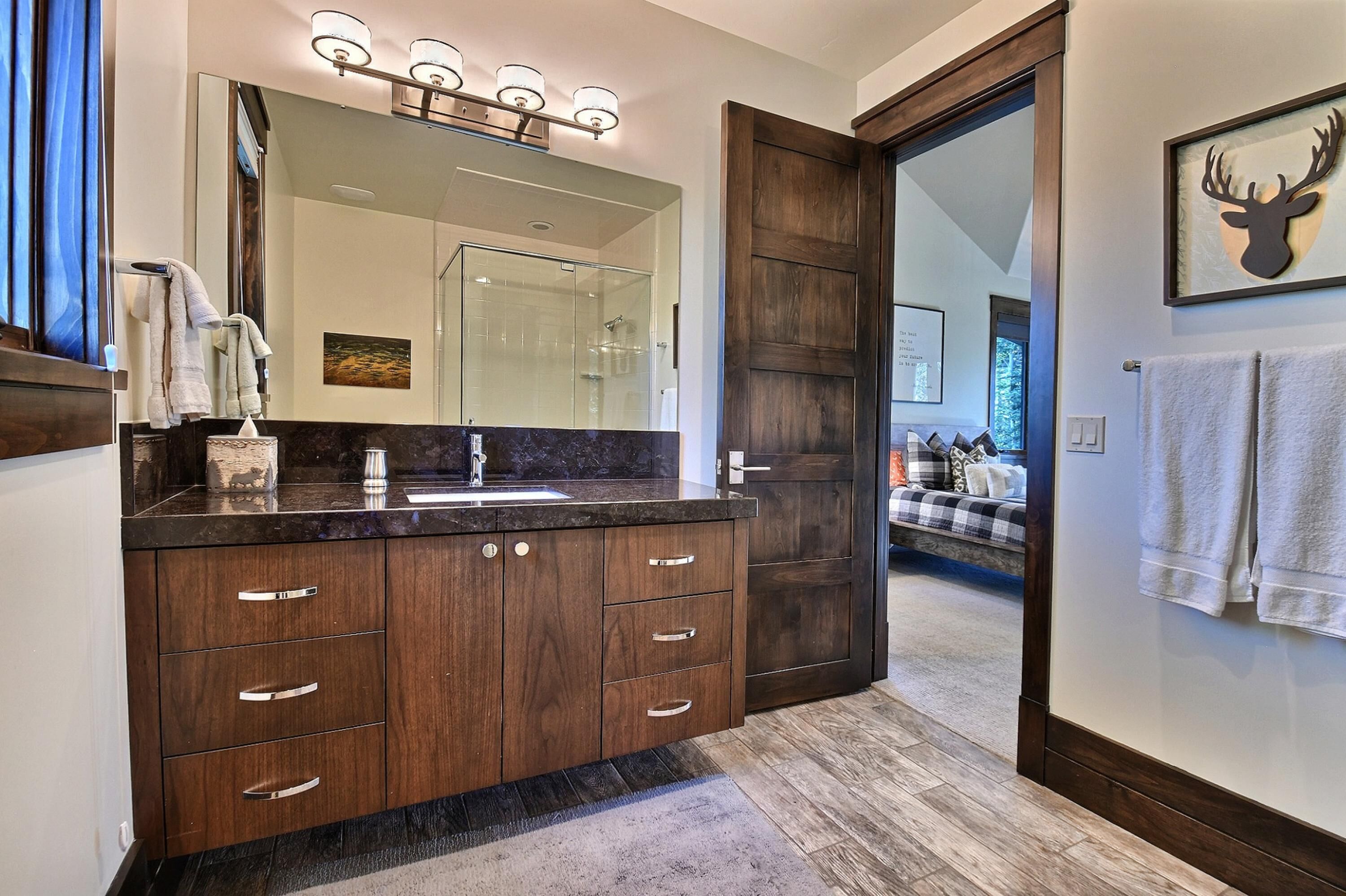 Un baño moderno con un espejo grande, muebles de madera oscura y zona de ducha.
