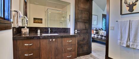 Un baño moderno con un espejo grande, muebles de madera oscura y zona de ducha.