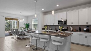 A modern kitchen with white cabinets, stainless steel appliances, and a central island with bar stools. - Luxury 6BR Villa w/ Private Pool • Disney (Davenport)