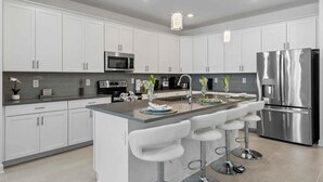 A modern kitchen with white cabinets, stainless steel appliances, and a central island with bar stools. - Luxury 6BR Villa w/ Private Pool • Disney (Davenport)