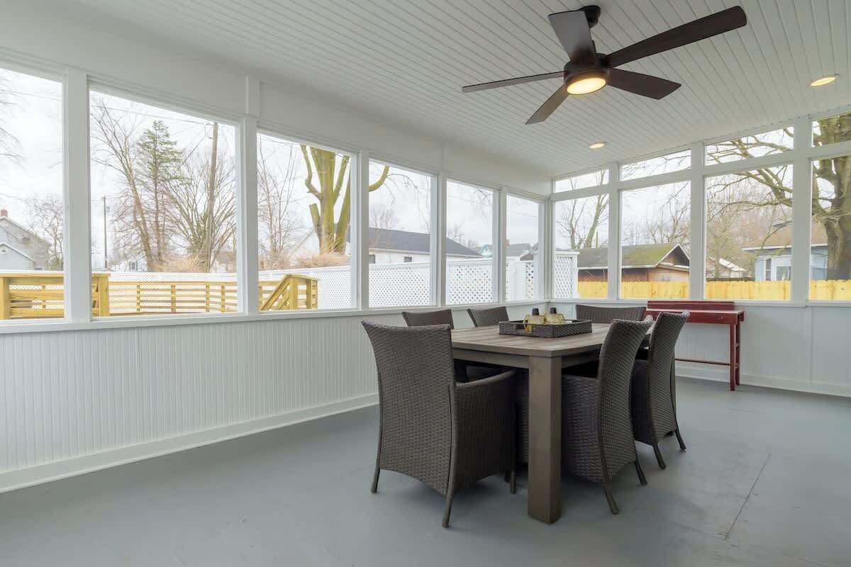 A sunroom with a dining table and chairs, large windows, and a ceiling fan.