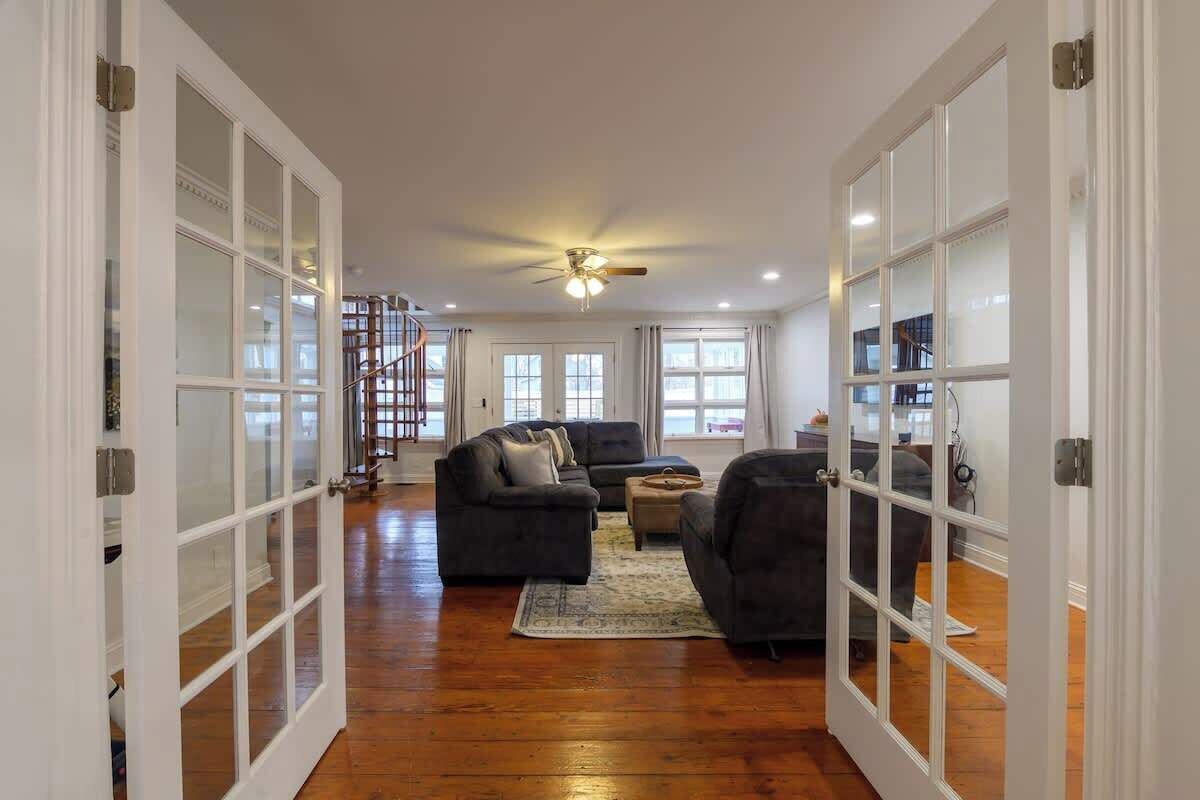 A spacious living room with a wooden floor, a ceiling fan, and a staircase leading to an upper level.