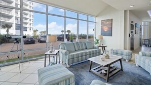 Ein geräumiger Wohnbereich mit großem Fenster, einer Couch, einem Couchtisch und Blick auf einen Parkplatz und Gebäude.