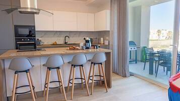 Uma cozinha moderna com ilha central, banquetas, forno embutido e vista para o pátio externo.