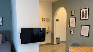A modern living room with a flat-screen TV mounted on the wall, a wooden table, a grey sofa, and a small archway leading to another room. - This apartment is a 1 bedroom(s), 1 bathrooms, located in Tas-Sliema, null. (Tas-Sliema)