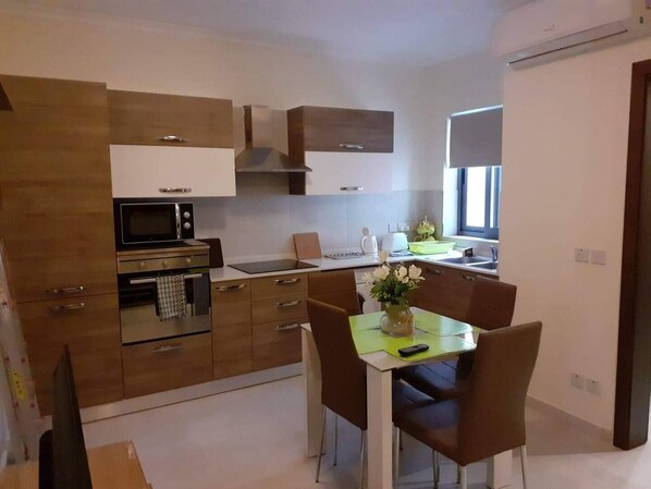 A modern kitchen with a dining area, featuring a microwave, oven, and a table with chairs.