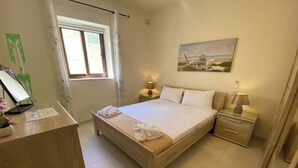 Un dormitorio con una cama, mesitas de noche, un escritorio con una computadora y un cuadro en la pared.