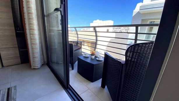 Ein Balkon mit Glastür, Korbmöbeln und Blick auf Gebäude.
