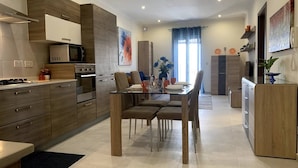 A modern kitchen with a dining area, featuring a central island, built-in appliances, and a large window with curtains.
