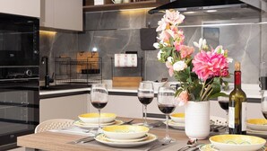 A modern kitchen with a dining table set for a meal, a bouquet of flowers, and a bottle of wine. - Modern 2-bedroom apartment in central Mellieħa. Sleeps 6 with sofa bed, A/C, Wi-Fi, Smart TV & lift access. Steps from shops, restaurants & public transport. (Il-Mellieħa)