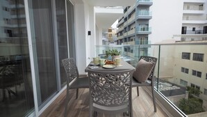 A balcony with a table, chairs, and potted plants. - Modern 2-bedroom apartment in central Mellieħa. Sleeps 6 with sofa bed, A/C, Wi-Fi, Smart TV & lift access. Steps from shops, restaurants & public transport. (Il-Mellieħa)