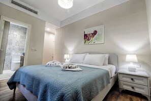 A modern hotel room with a large bed, two bedside tables with lamps, a painting on the wall, and a bathroom visible through an open door. - Relax with the whole family at this peaceful place to stay (Il-Mellieħa)