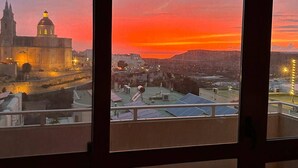 A view from a window overlooking a cityscape at sunset, featuring a prominent cathedral and surrounding buildings.