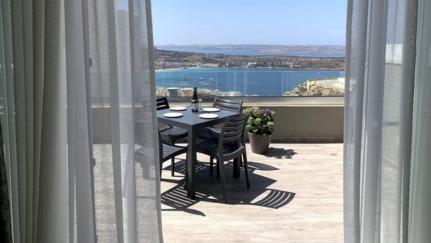 Ein Balkon mit Esstisch, der auf eine Küstenlandschaft blickt.