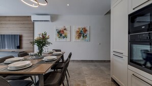 Eine moderne Küche mit Essbereich, mit einem Holztisch für vier Personen, einem eingebauten Backofen und abstrakter Kunst an der Wand.