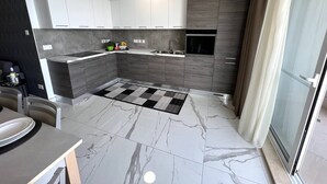 Une cuisine moderne avec des meubles gris, un tapis noir et blanc et un sol en marbre.
