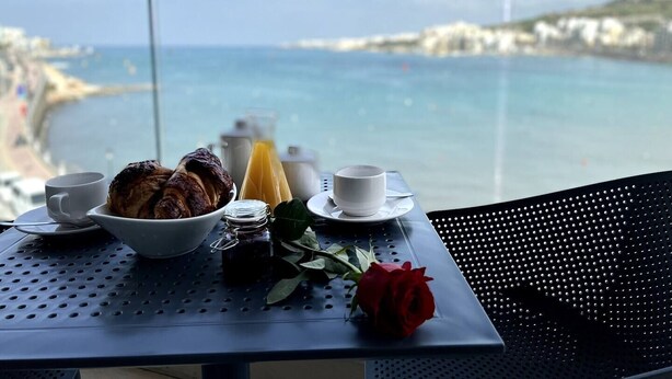 Une table avec des aliments pour le petit-déjeuner, une rose et une vue sur la mer et la côte.