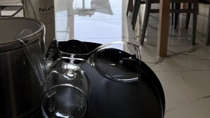 Une table à manger avec des verres à vin et une bouteille de vin, une chaise, et une vue sur la mer par une porte vitrée.