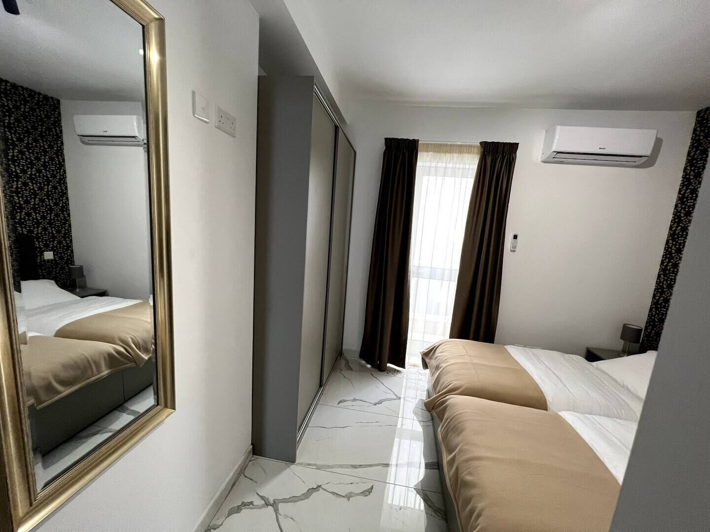 Hotellihuone, jossa on suuri peili, kaksi sänkyä, vaatekaappi ja ilmastointilaite.