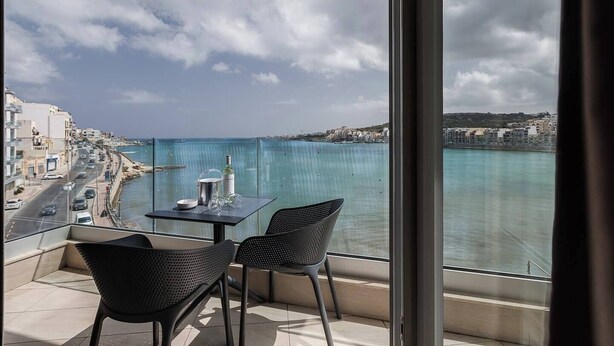 A balcony with a table and chairs overlooking a coastal view. - Kick back and relax in this calm, stylish space (San Pawl il-Baħar)
