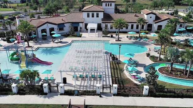 A large swimming pool with a slide, surrounded by lounge chairs and umbrellas. - Themed 8BR | Arcade | 2 Theaters | Pool & Spa (Kissimmee)