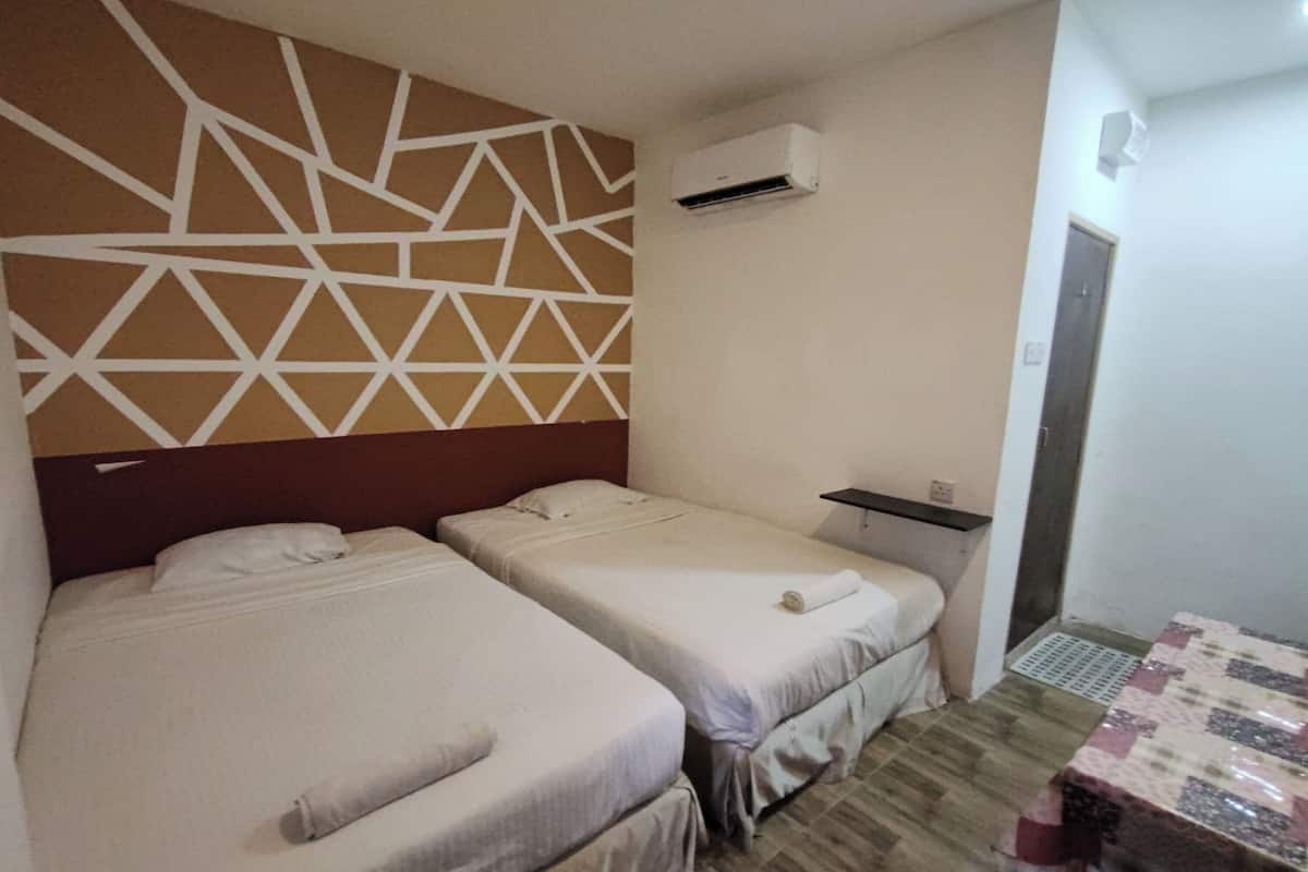 A hotel room with two single beds, a wall-mounted air conditioner, a small table, and a patterned rug.
